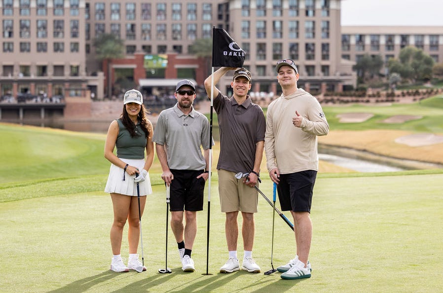 Group of four individuals posing on a golf course with a flag.