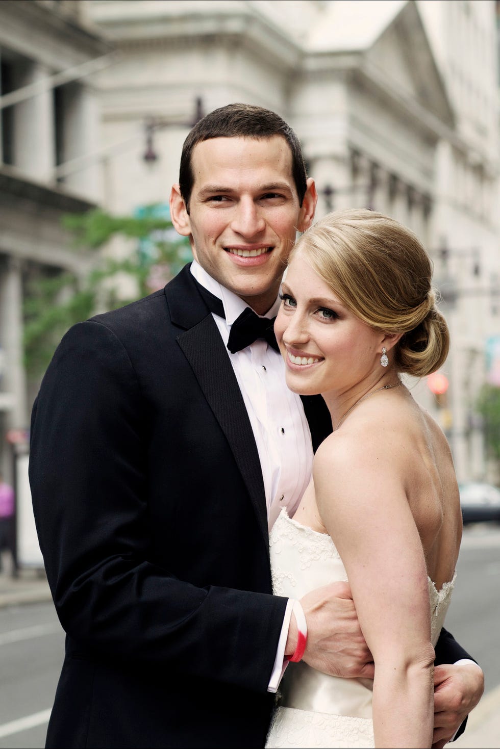 Couple in formal attire embracing on a city street.