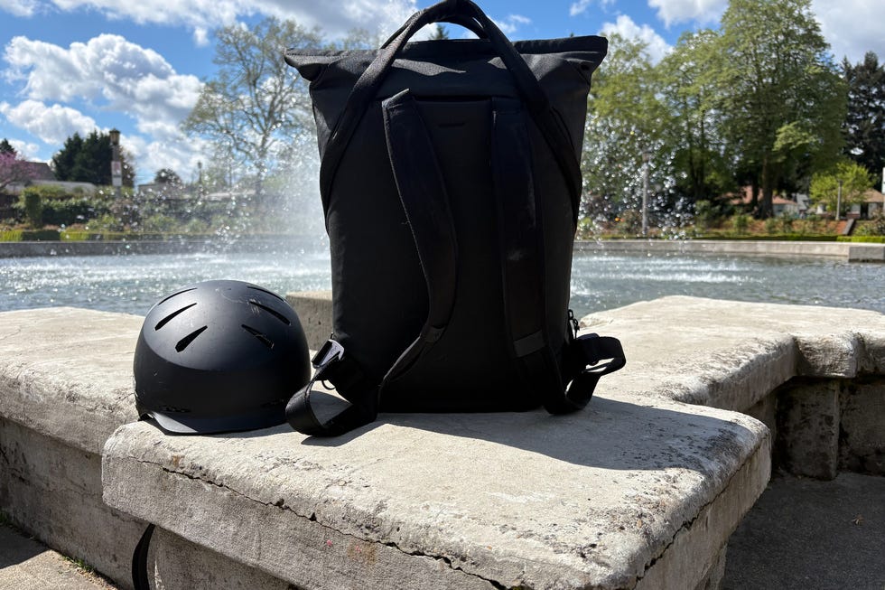A black backpack and a helmet placed on a stone surface near water.