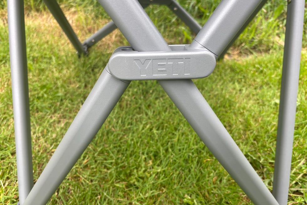 A close-up view of a gray folding chair's leg mechanism with a logo.
