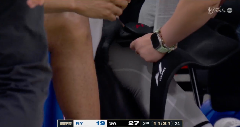 Person adjusting a HyperIce device on a seated athlete during a basketball game, second quarter score NY 19 - SA 27.