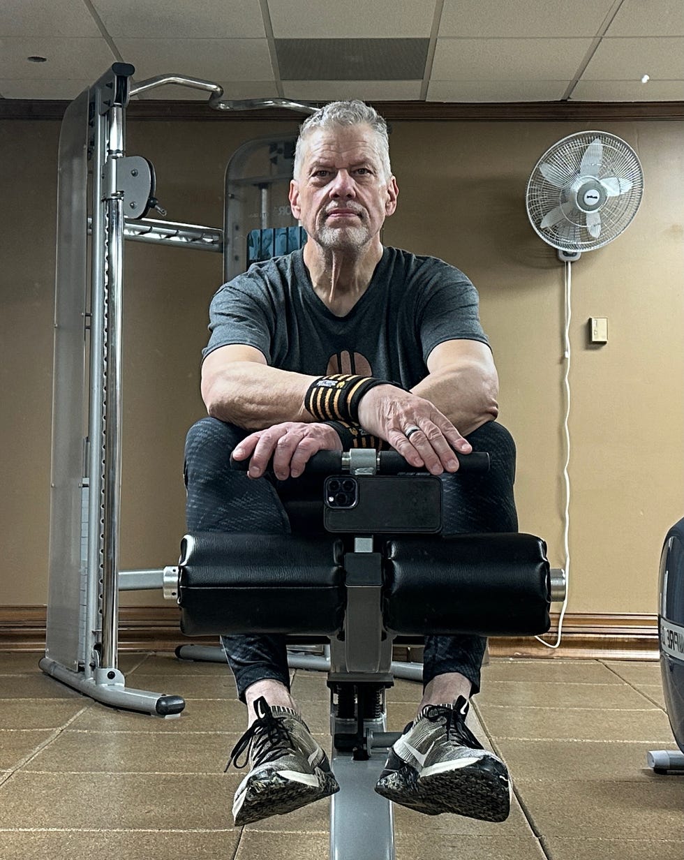 Glen Wagner sitting on gym equipment, facing camera, with workout gear and wristbands.