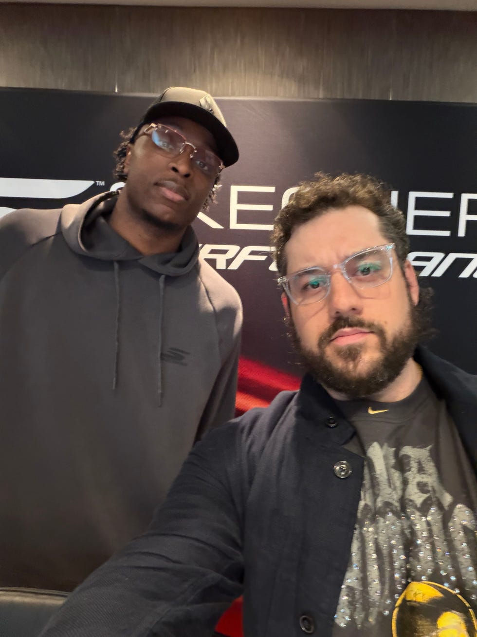 Two individuals posing for a selfie in front of a branded backdrop.