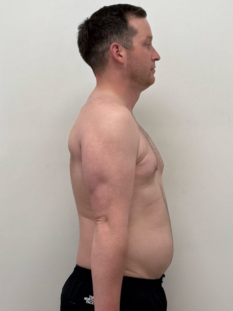 Bran Hughes standing sideways, exposing torso against a plain backdrop.