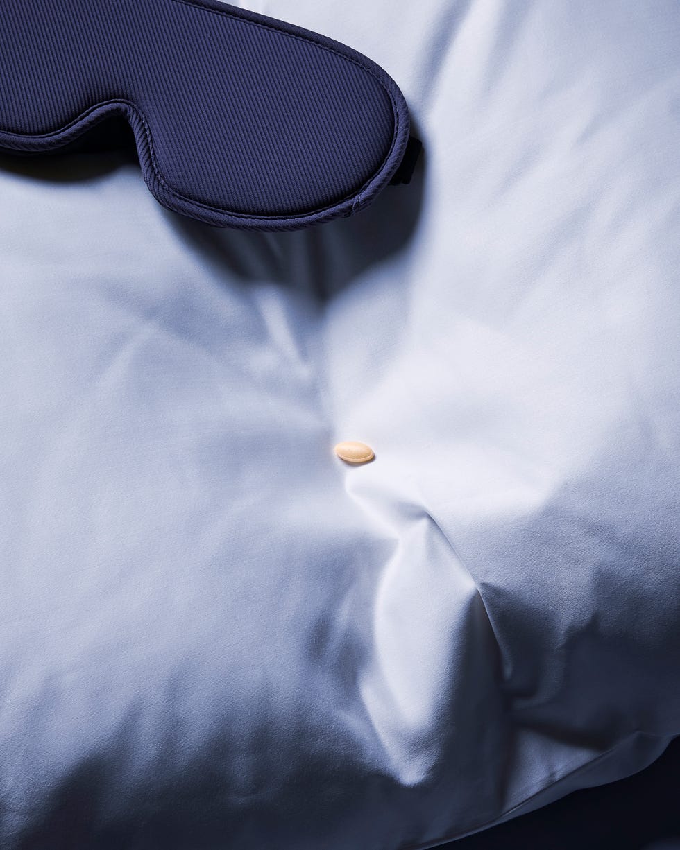 A dark sleep mask resting on a light blue pillow with a small pill nearby. A dark sleep mask resting on a light blue pillow with a small pill nearby.