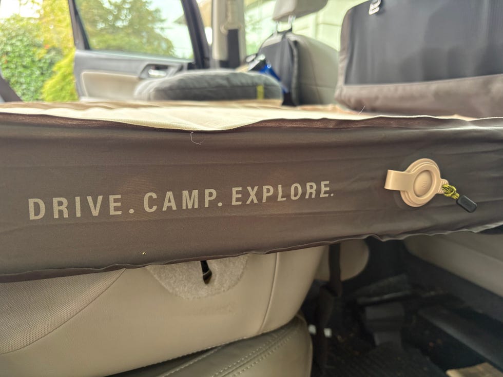 Camping mattress with "DRIVE. CAMP. EXPLORE." text, placed in the back seat of a vehicle.