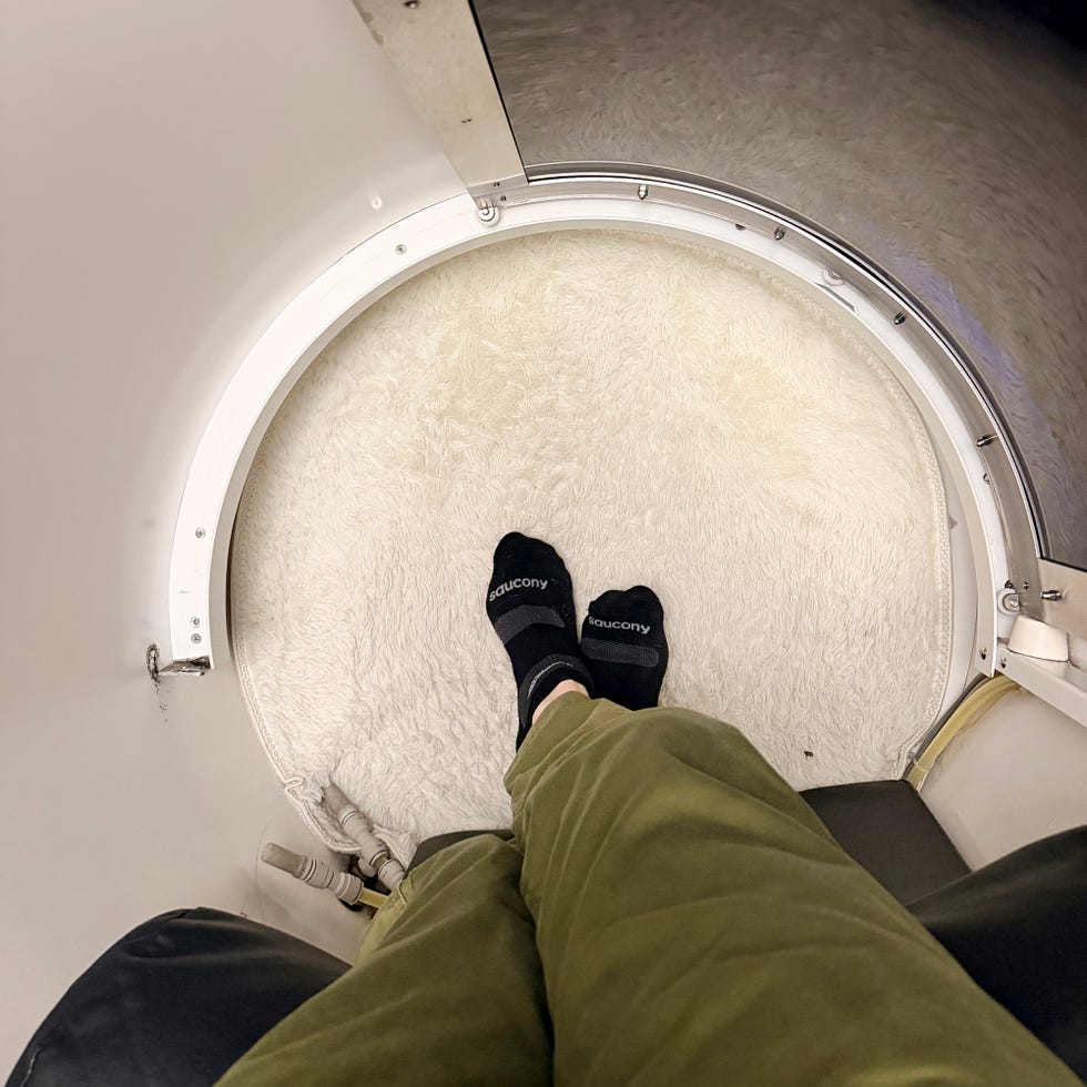 Feet in black socks resting on a plush round rug inside a small enclosed space.