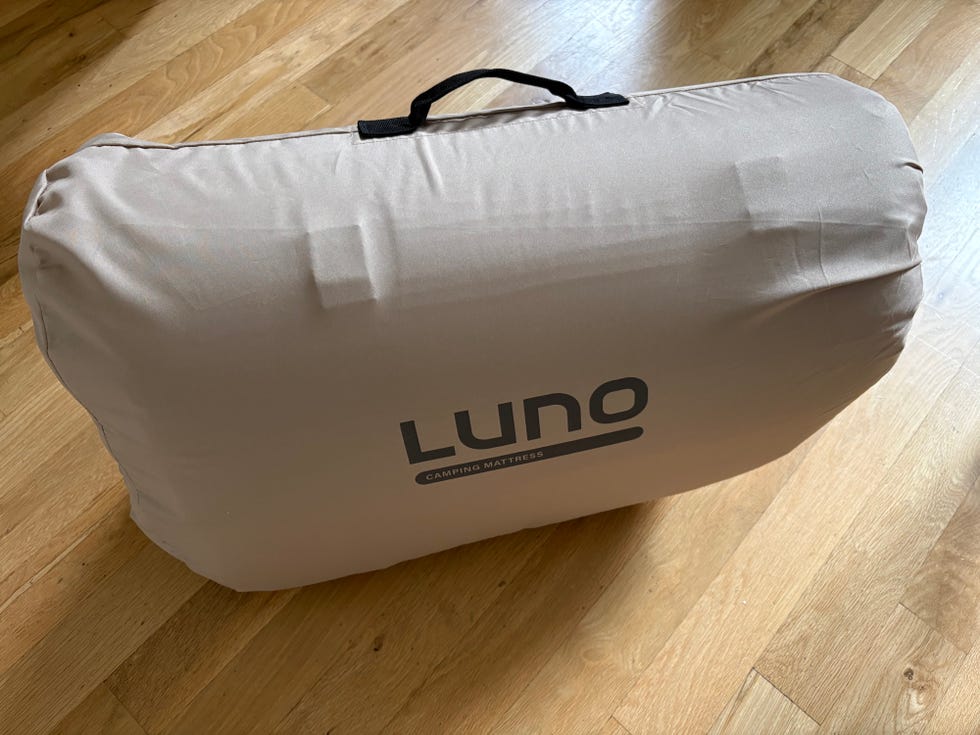 Luno camping mattress in a storage bag, with a handle, on a wooden floor background.