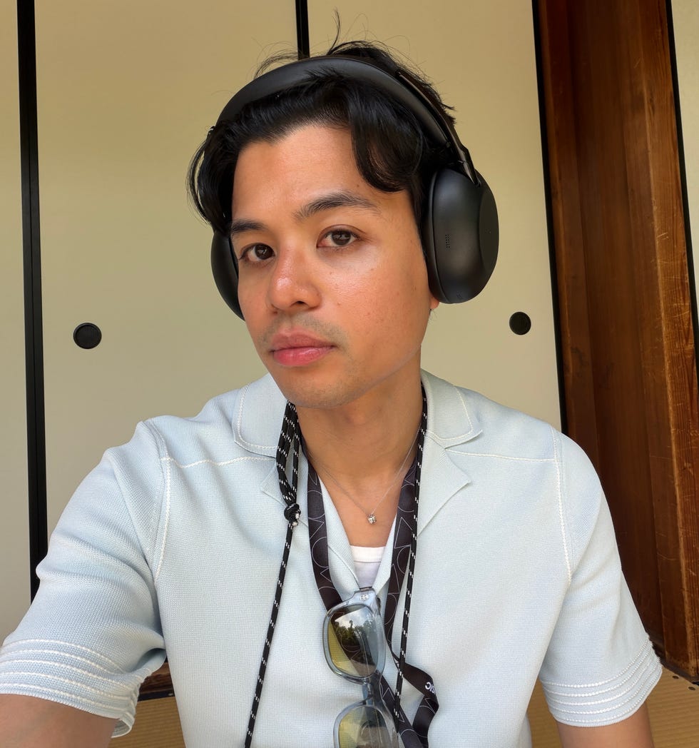 Person wearing headphones and sunglasses, posing indoors in a light blue shirt with a casual style.