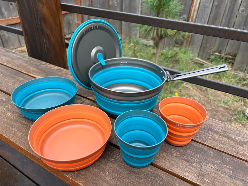 Set of collapsible cookware and bowls in blue and orange on a wooden table.