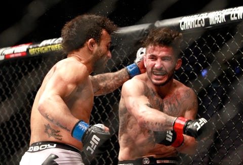 Two fighters engaging in a mixed martial arts match inside the octagon, one delivering a punch to the other.