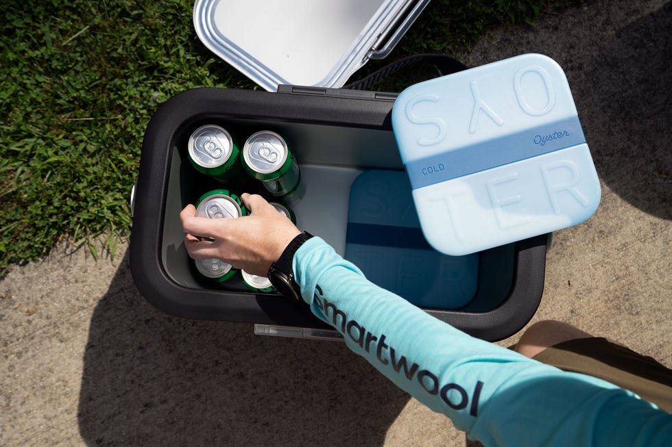 A person reaching into a cooler filled with cans and a blue ice pack on top.