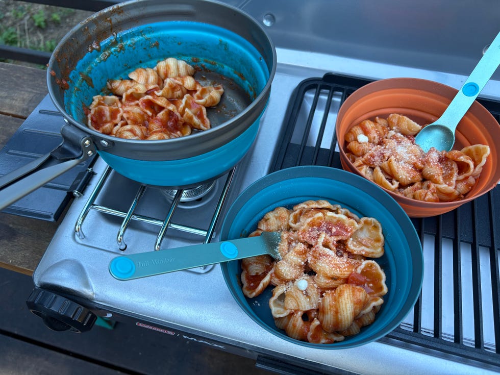 Pasta with sauce served in bowls on a camping stove in an outdoor setting.