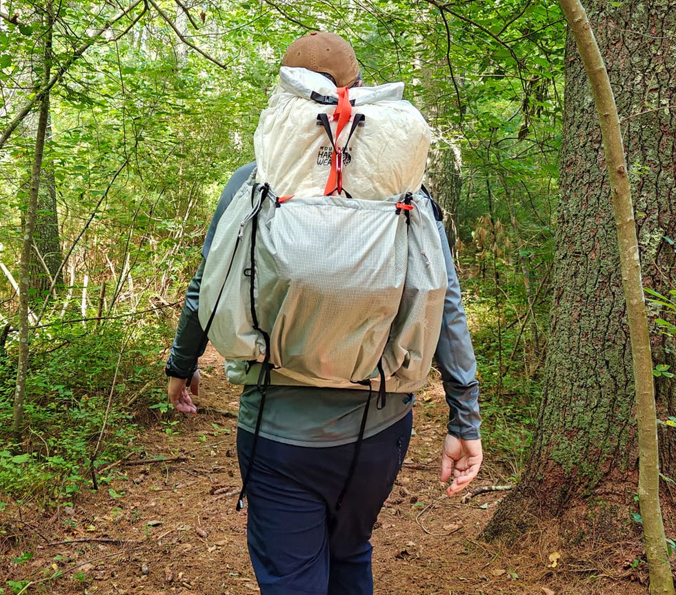 Person hiking on a forest trail, wearing a large backpack, surrounded by lush greenery and trees.