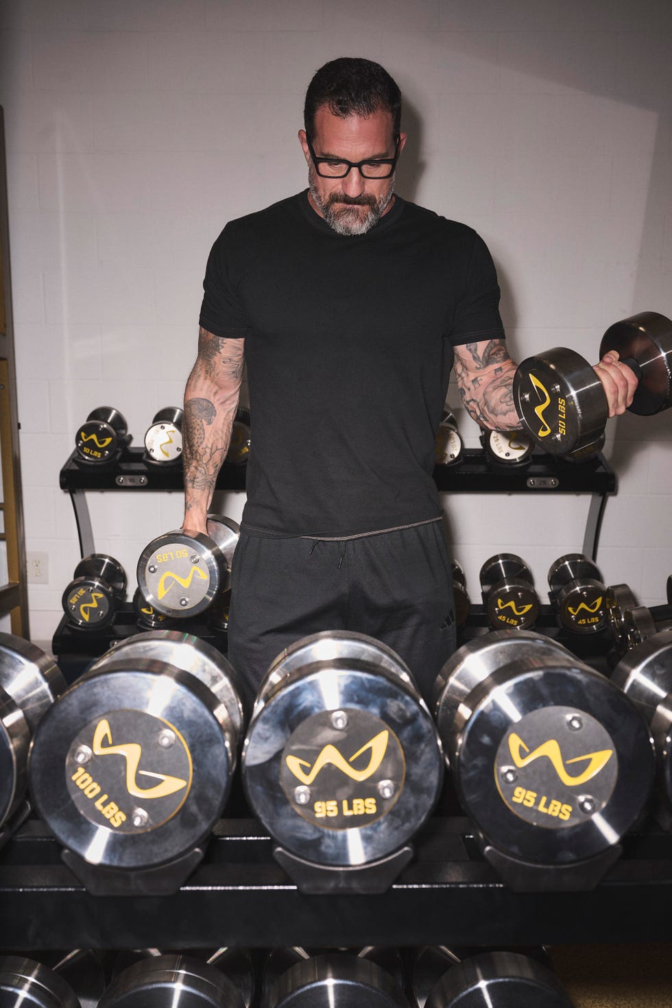 Man in a gym holding a 95-pound dumbbell with various weights in the background.