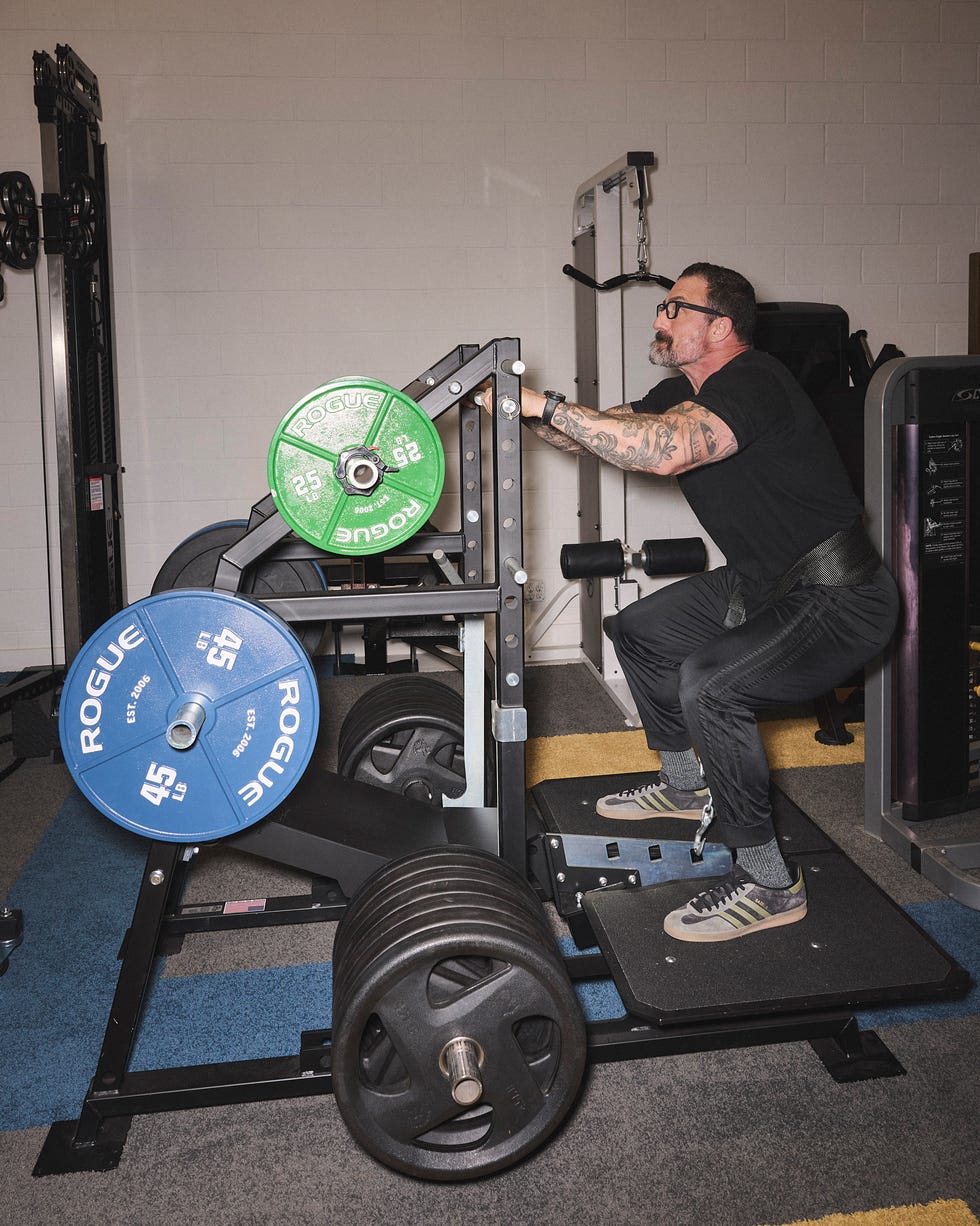 Man performing squats using a weightlifting machine in a gym setting.