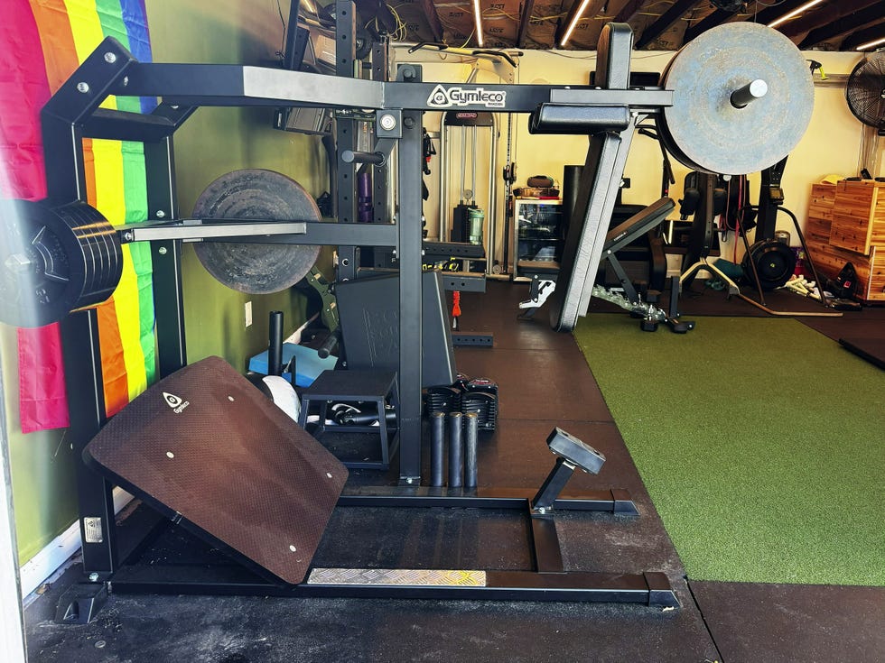 Weightlifting equipment in a home gym with a rainbow flag hanging on the wall.