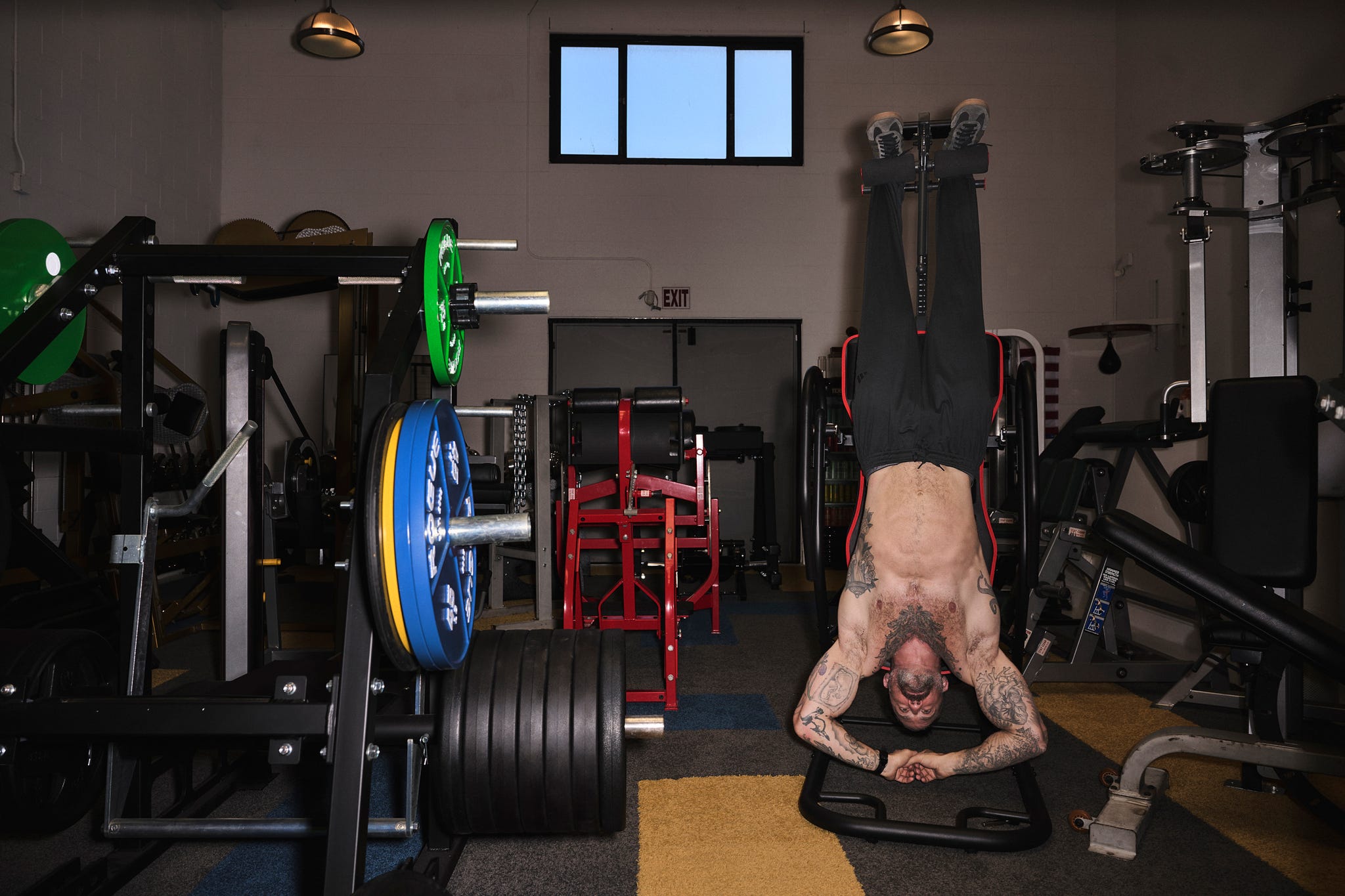 Athlete performing an inverted exercise in a gym setting with various weightlifting equipment in the background.