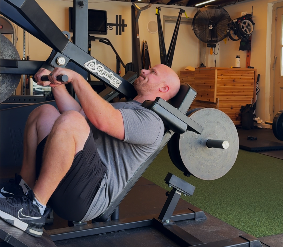 Man exercising on a leg press machine in a gym with weights.